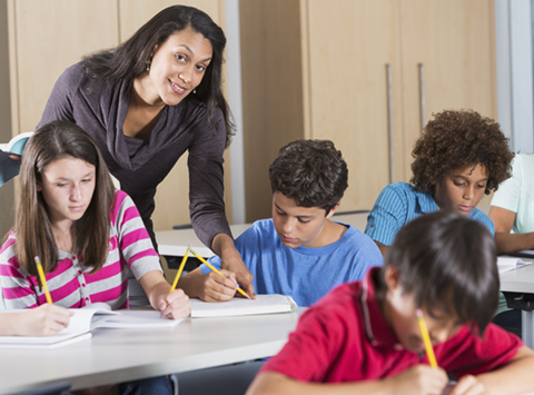 Multi-ethnic group of students with teacher in classroom. Main focus on teacher.